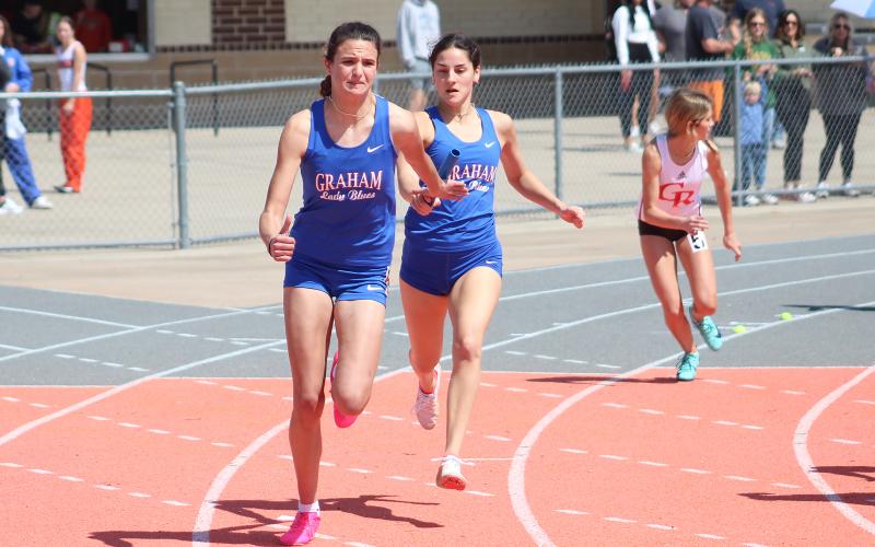 (TC GORDON | THE GRAHAM LEADER) Georgia Martin (right) passes the baton to teammate Sophie Schlieper (left) during one of the relays at a meet earlier this season. The two Lady Blues were part of the relay teams that qualified for the regional meet after competing in the area meet in Abilene last Friday, April 12.
