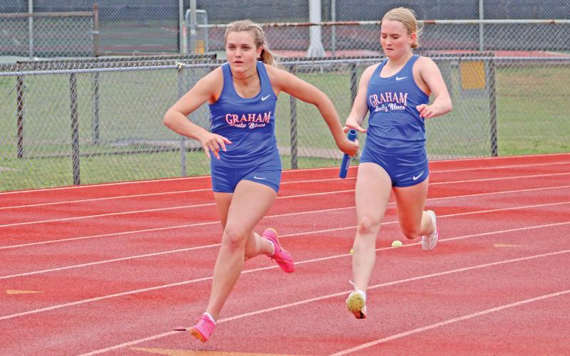 (TC GORDON | THE GRAHAM LEADER) Graham’s Olivia Pettus (right) passes off the baton to teammate Kaden Atwood (left) during a running relay at a track meet earlier this season.